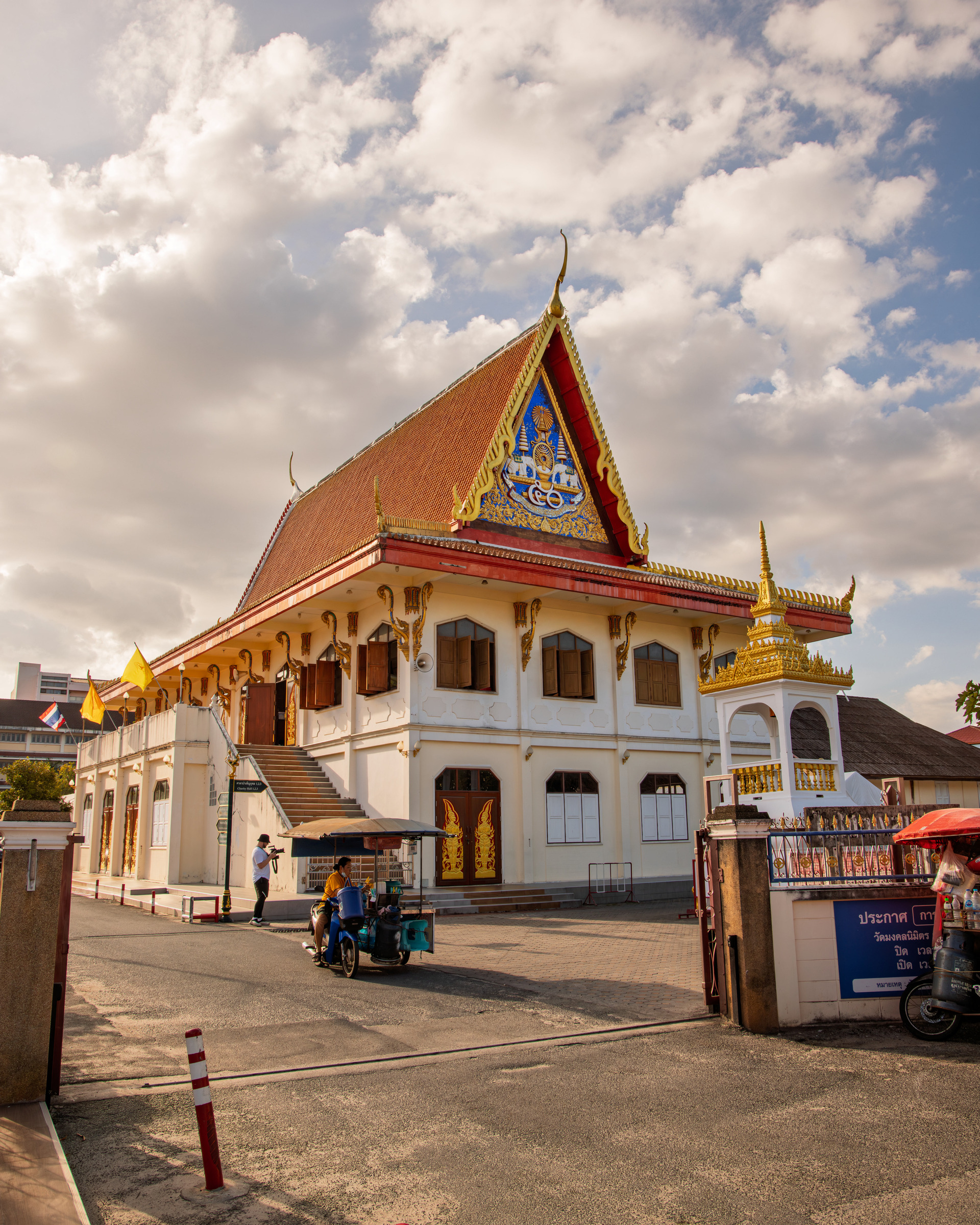 Thai Buddhist temple with ornate gable, orange-tiled roof and gilded naga finials under dramatic clouds — architectural photography by Samuel John Ford