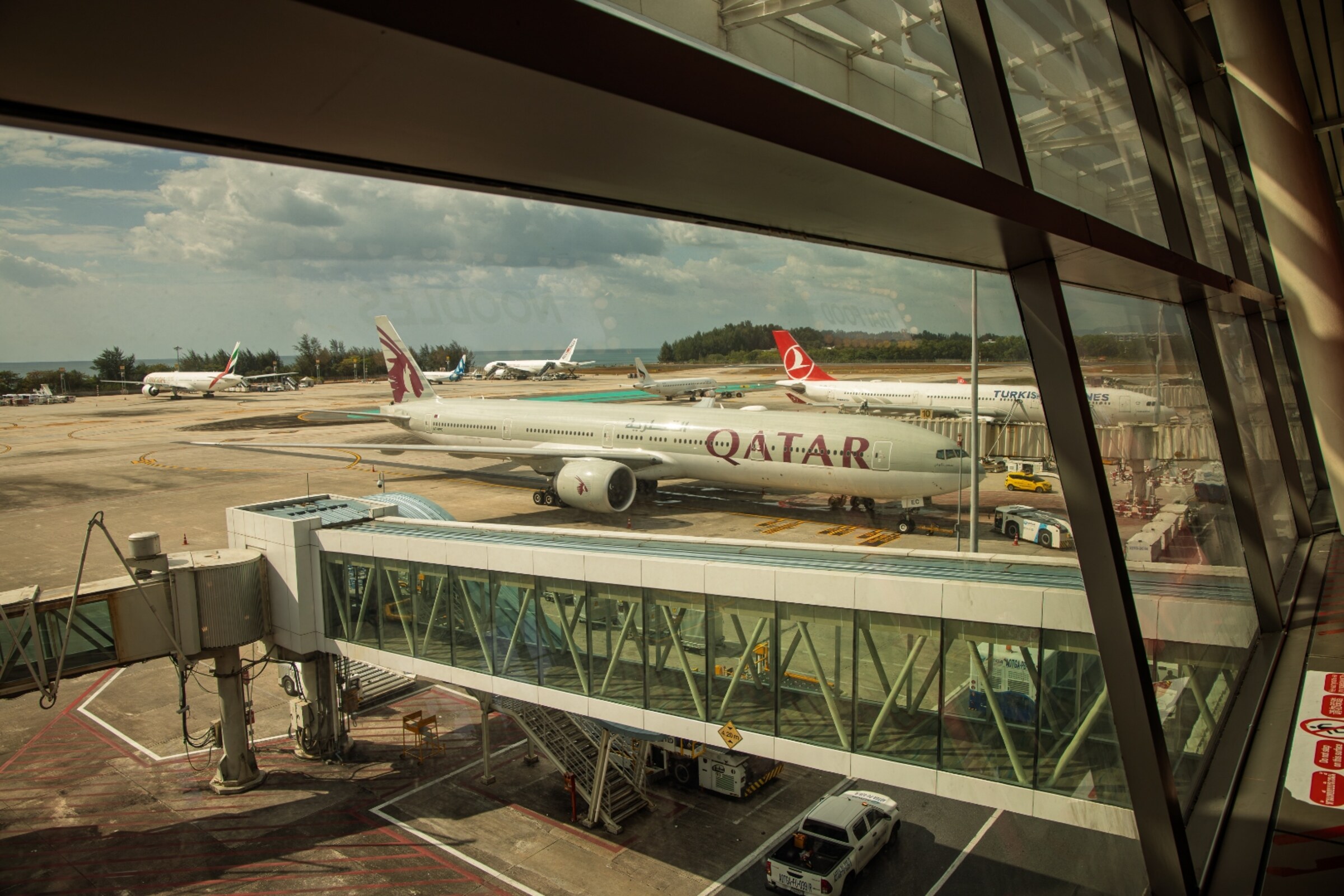 Qatar Airways Boeing 777 and Turkish Airlines aircraft at Phuket International Airport seen through terminal window — travel photography