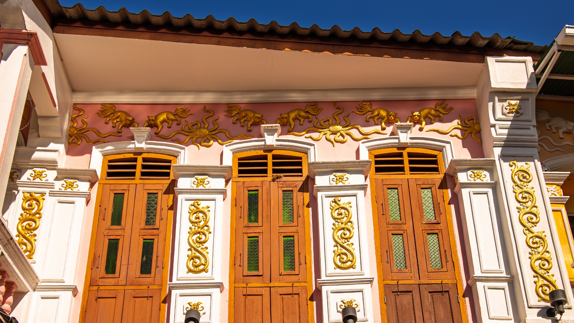 Golden mythological creatures and ornate shutters on pink Sino-Portuguese facade, Phuket Town — architectural detail photography