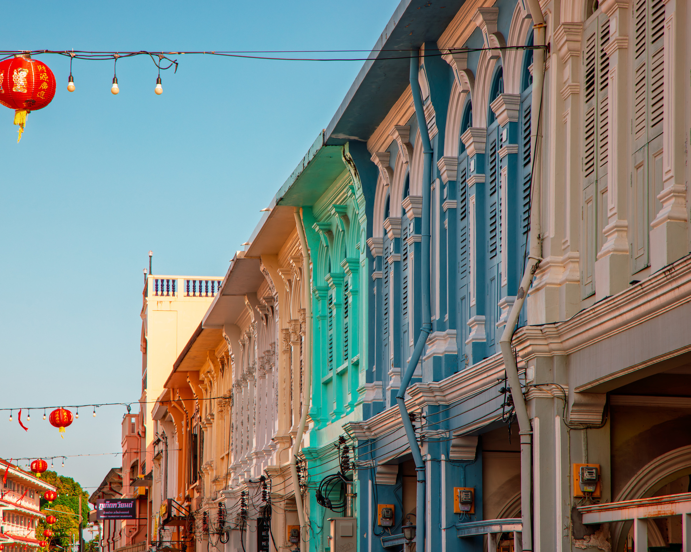 Row of colourful Sino-Portuguese shophouse facades in blue, green, cream and pink with red lanterns, Phuket Old Town — architectural photography