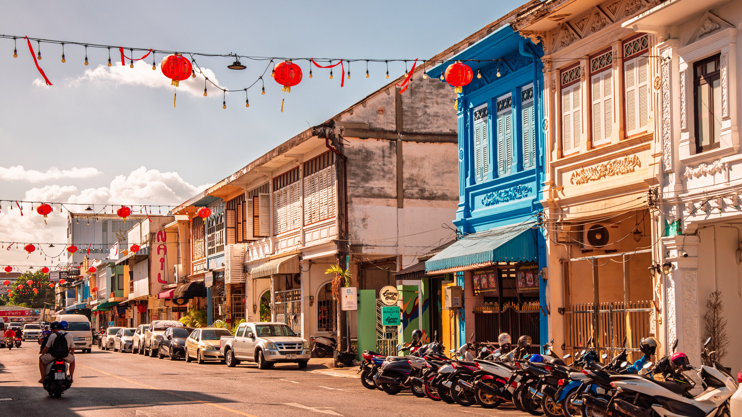 Phuket Old Town street with red lanterns, blue shophouse and motorbikes under golden afternoon light — architectural street photography