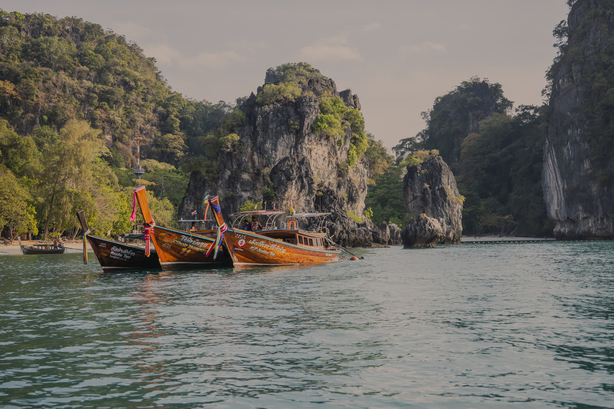 Traditional longtail boats moored beside limestone cliffs, Krabi, Thailand — landscape photography by Samuel John Ford