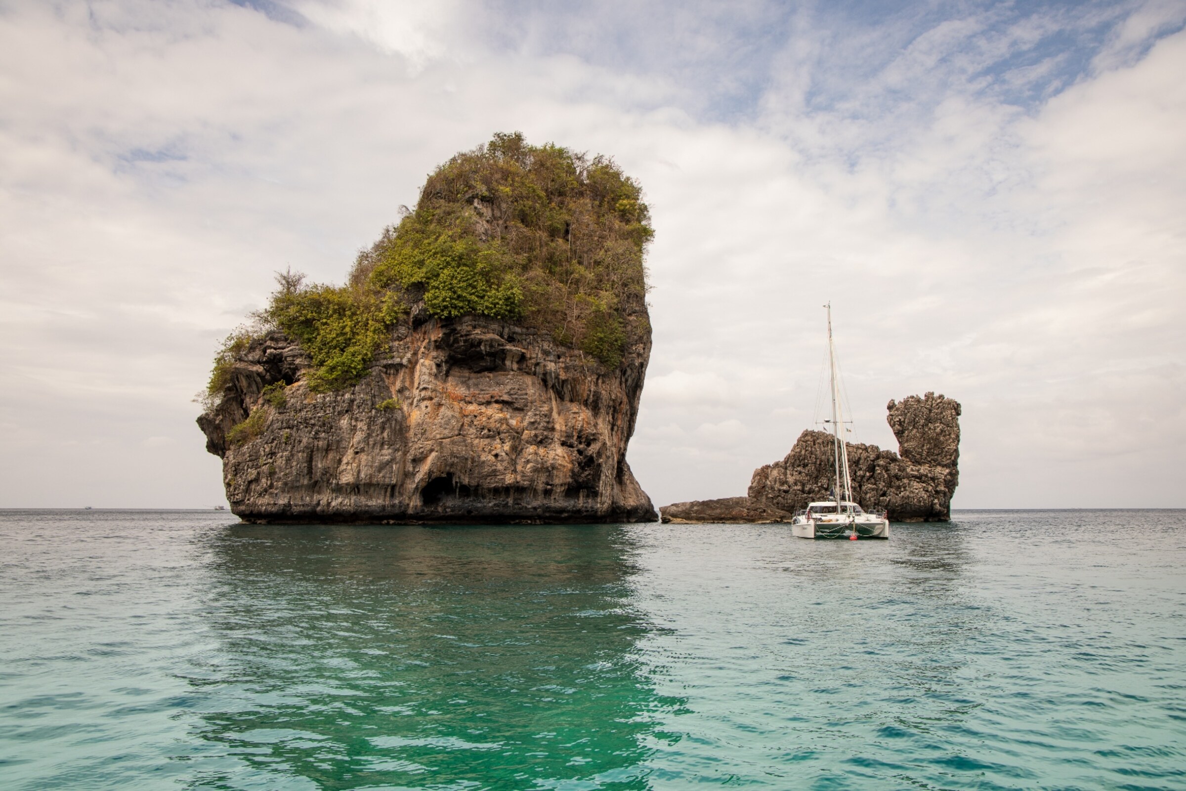 Limestone karst and small rock stack in emerald green sea with a catamaran, Andaman Sea — seascape photography by Samuel John Ford