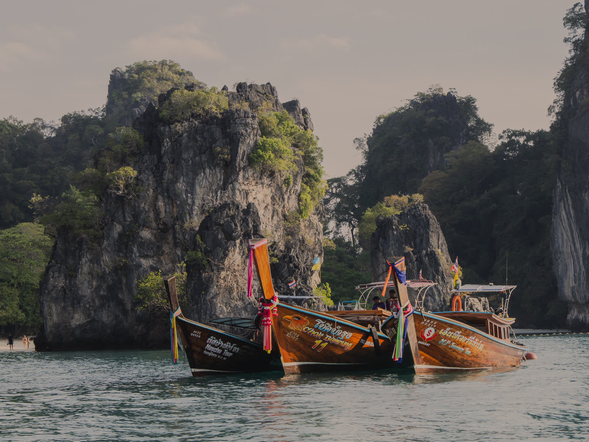 Traditional Thai longtail boats with colourful ribbons moored before towering limestone karst islands, Krabi — landscape photography by Samuel John Ford