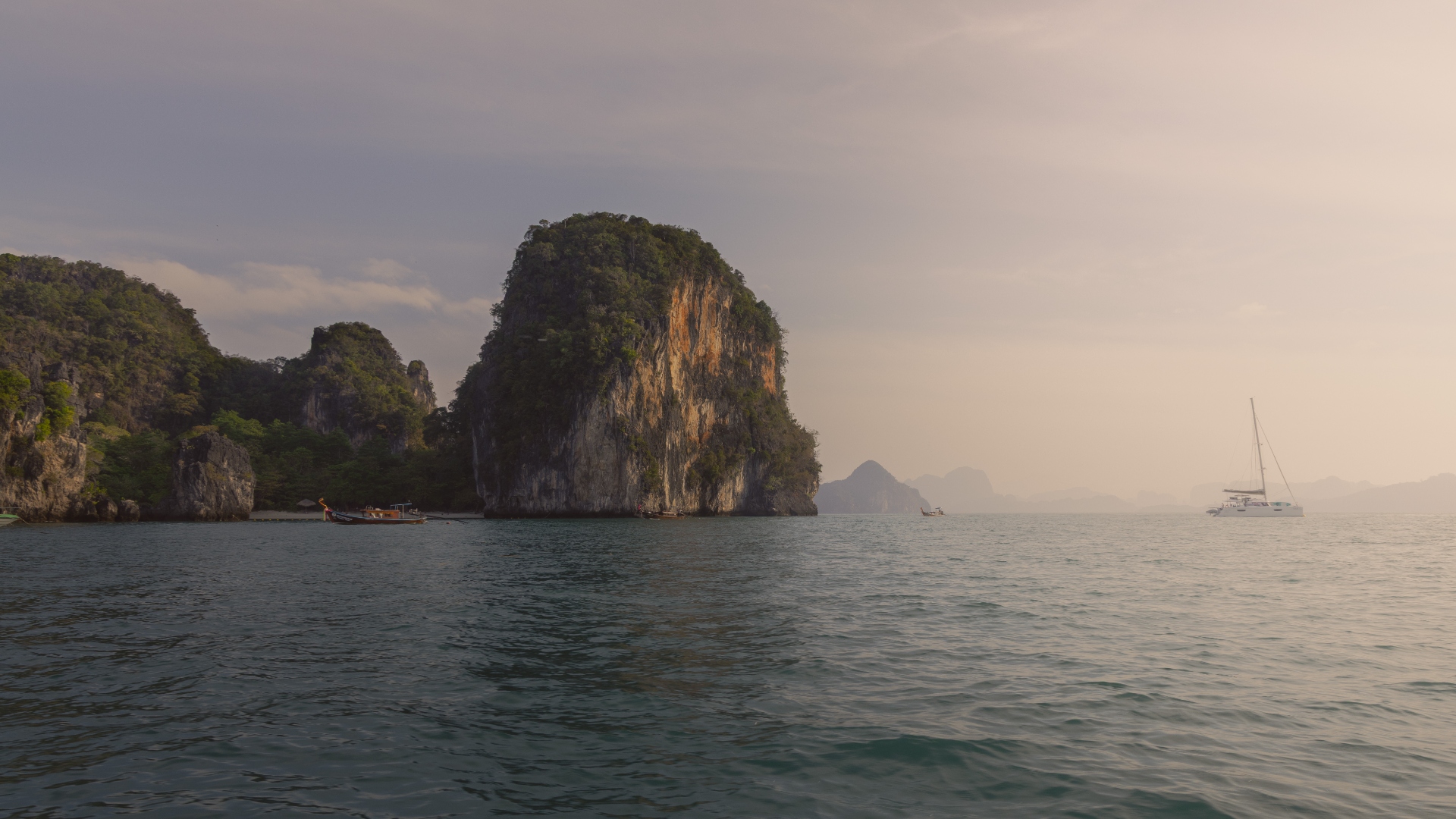 Limestone karst island rising from the Andaman Sea at sunset with a distant catamaran, Thailand — landscape photography