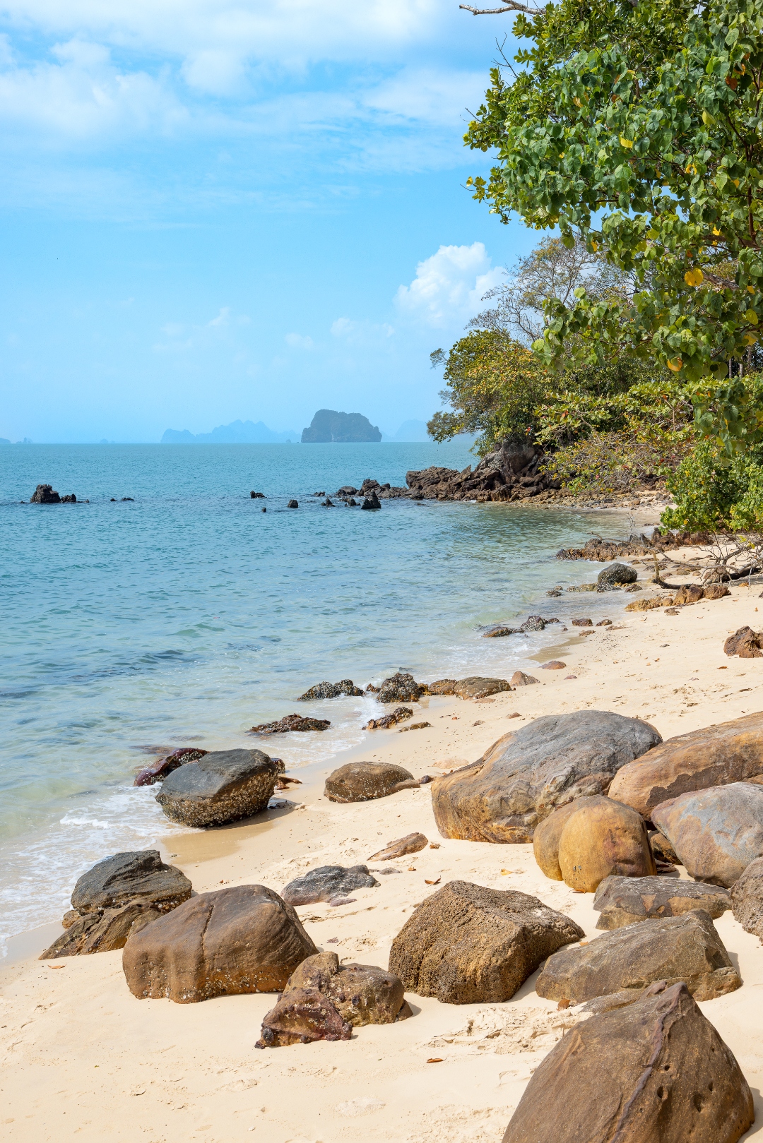 Secluded white-sand beach with boulders, tropical trees and distant islands on a clear day — landscape photography by Samuel John Ford