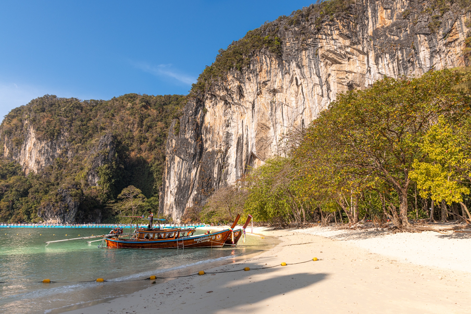 Longtail boats on white sand beneath a towering limestone cliff, Phi Phi Islands, Thailand — travel photography