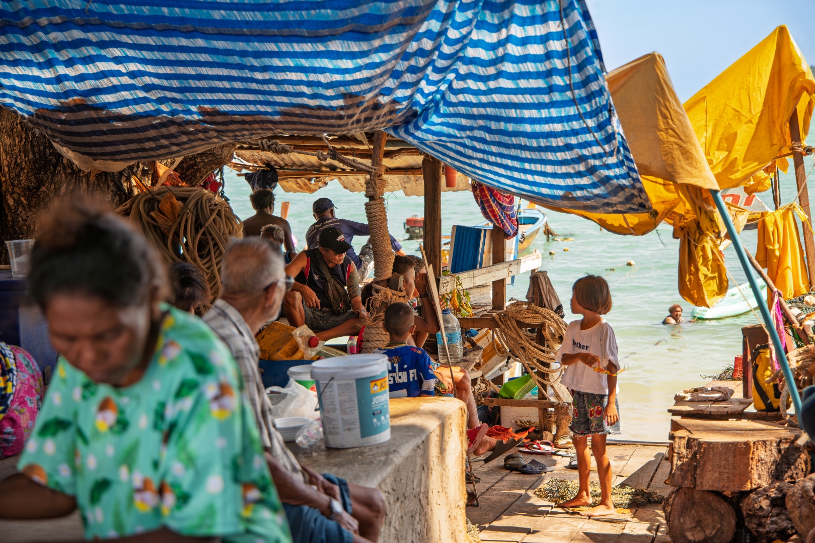 Harbourside community under blue tarps with children and fishing boats, Thai coastal village — travel photography