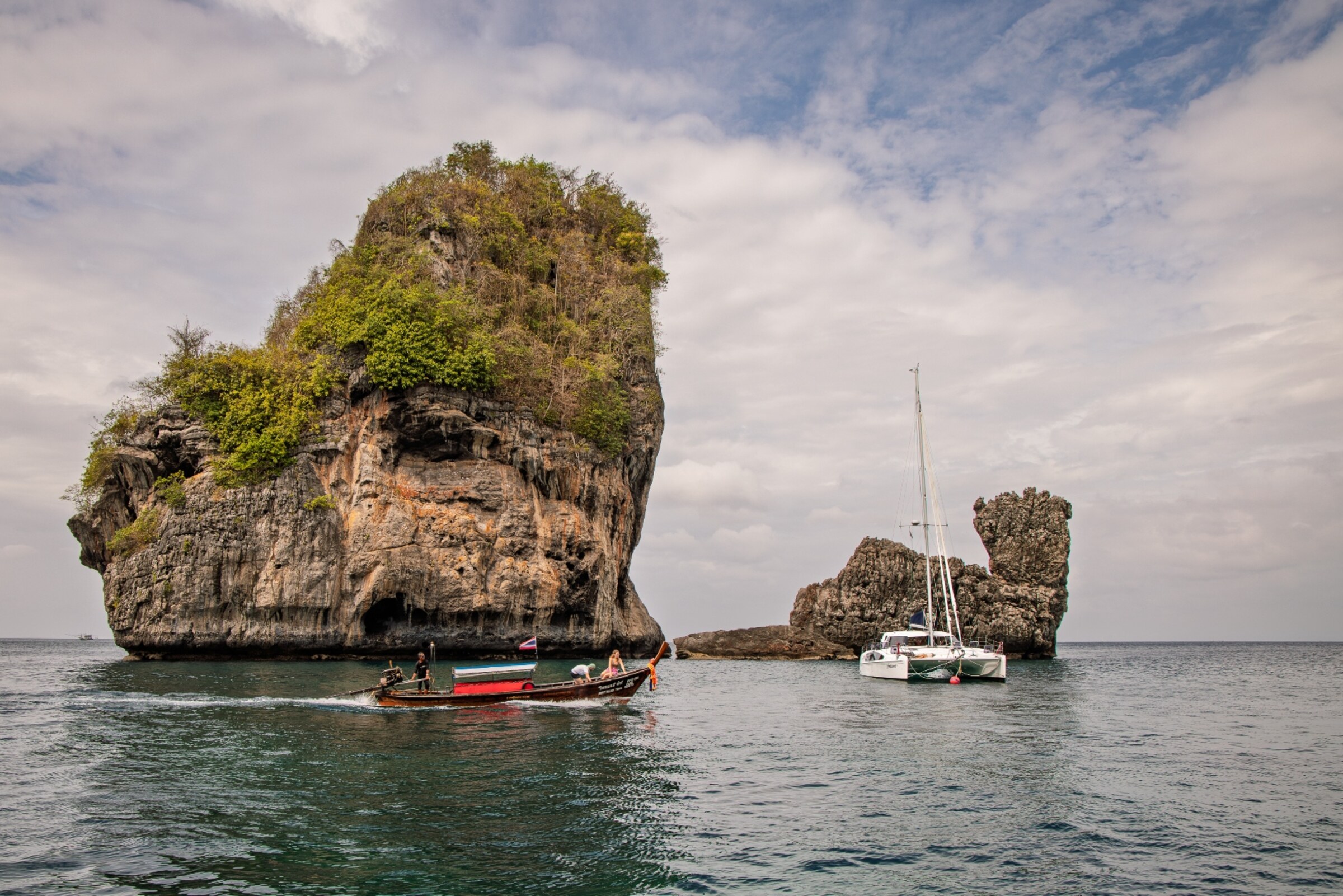 Longtail boat and white catamaran beside a dramatic limestone karst island in the Andaman Sea — travel photography by Samuel John Ford