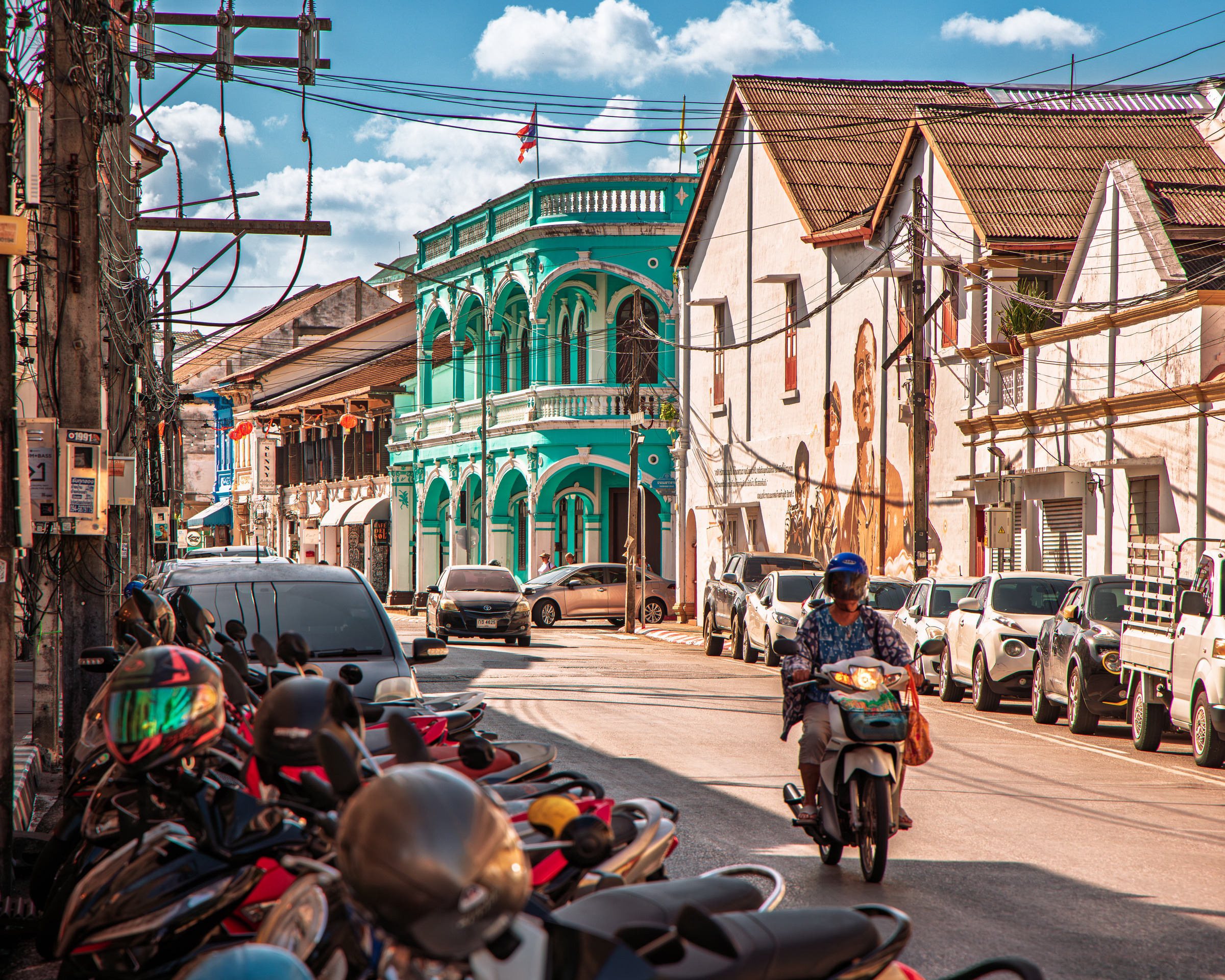 Phuket Old Town street scene with turquoise Sino-Portuguese corner building, mural art and motorbike rider — street photography