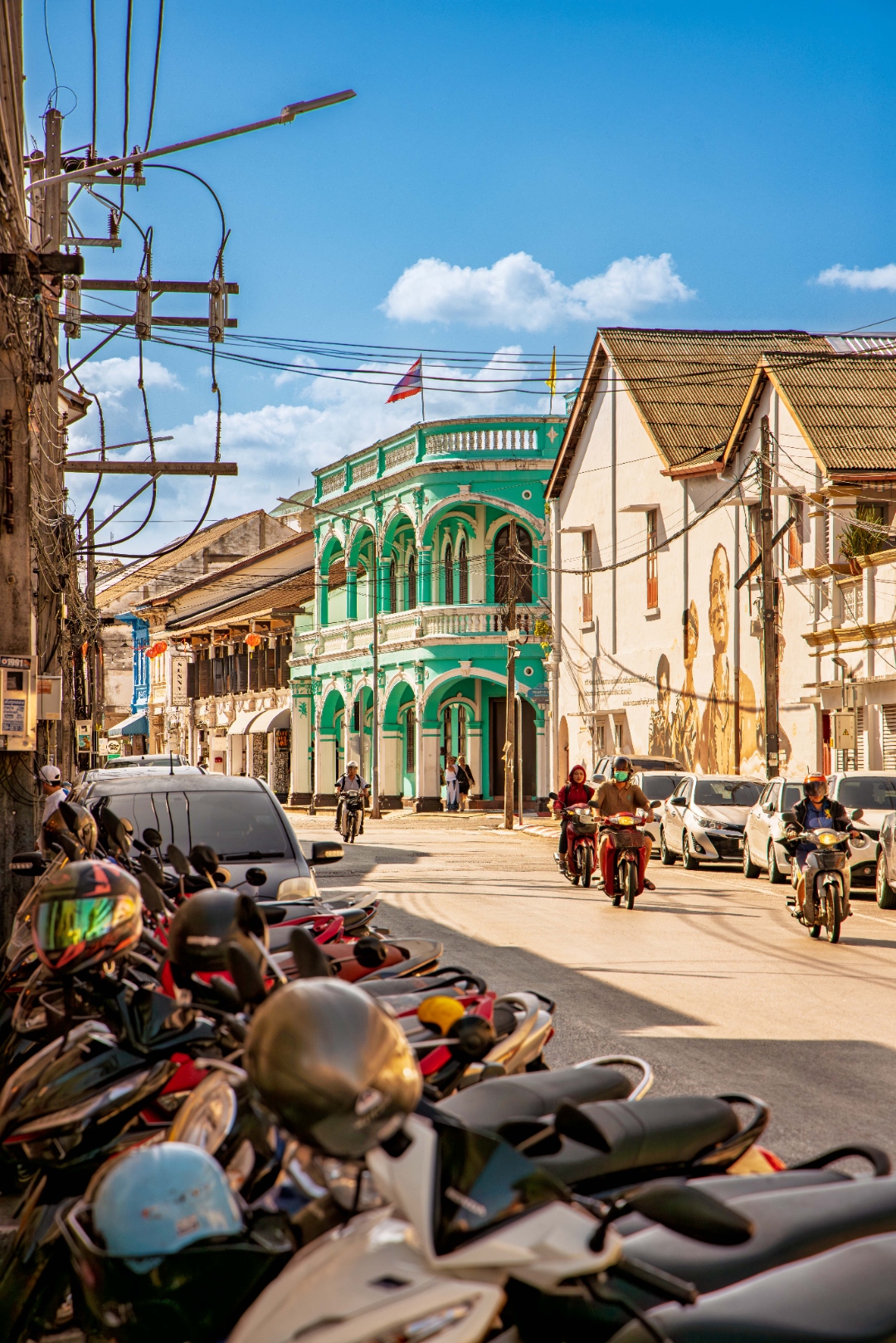 Busy Phuket Old Town street with turquoise Sino-Portuguese corner building, mural, motorbikes and colourful scooters — street photography